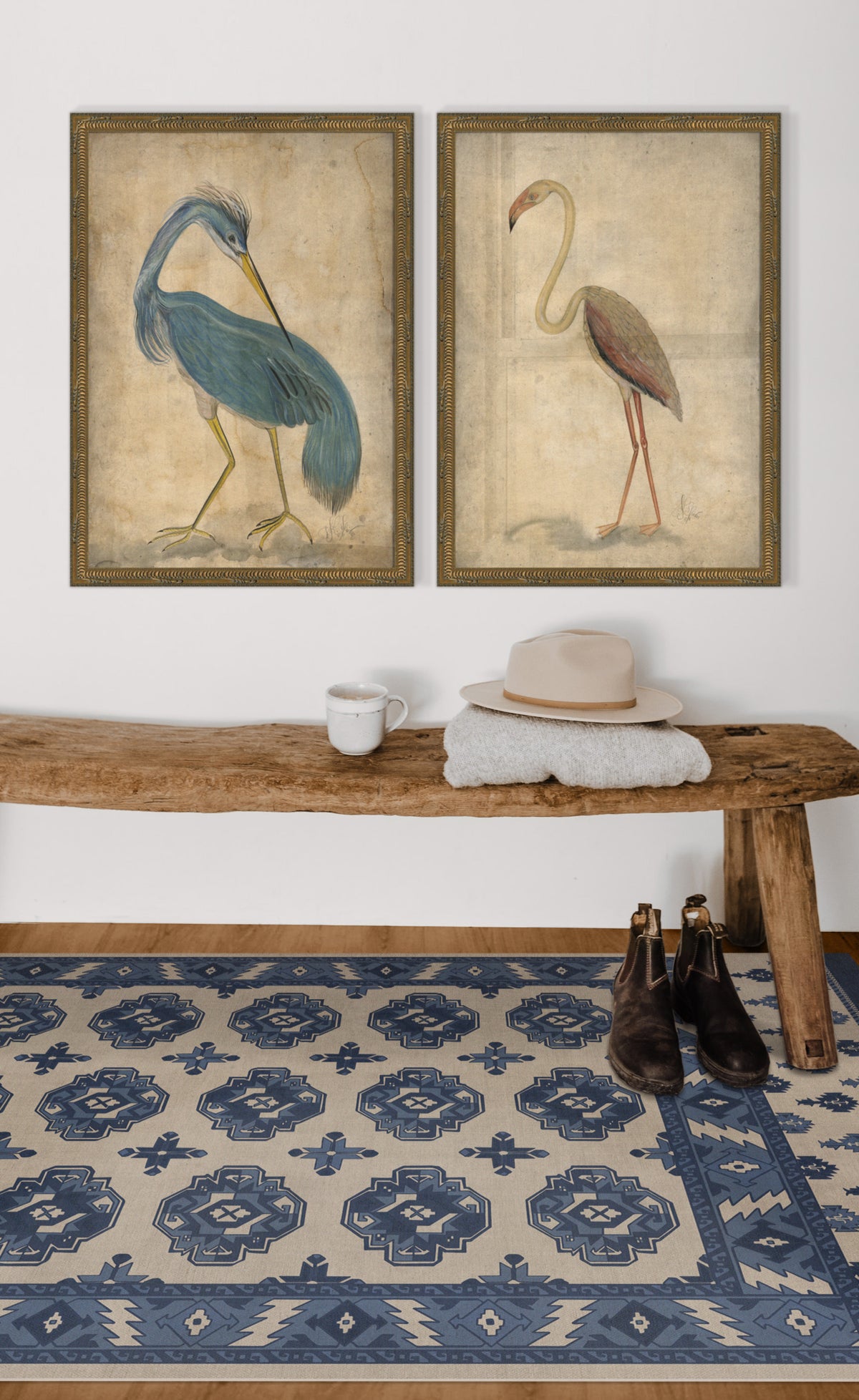 Framed artwork of a heron and a flamingo above a wooden bench with a hat, mug, and boots on a patterned rug.